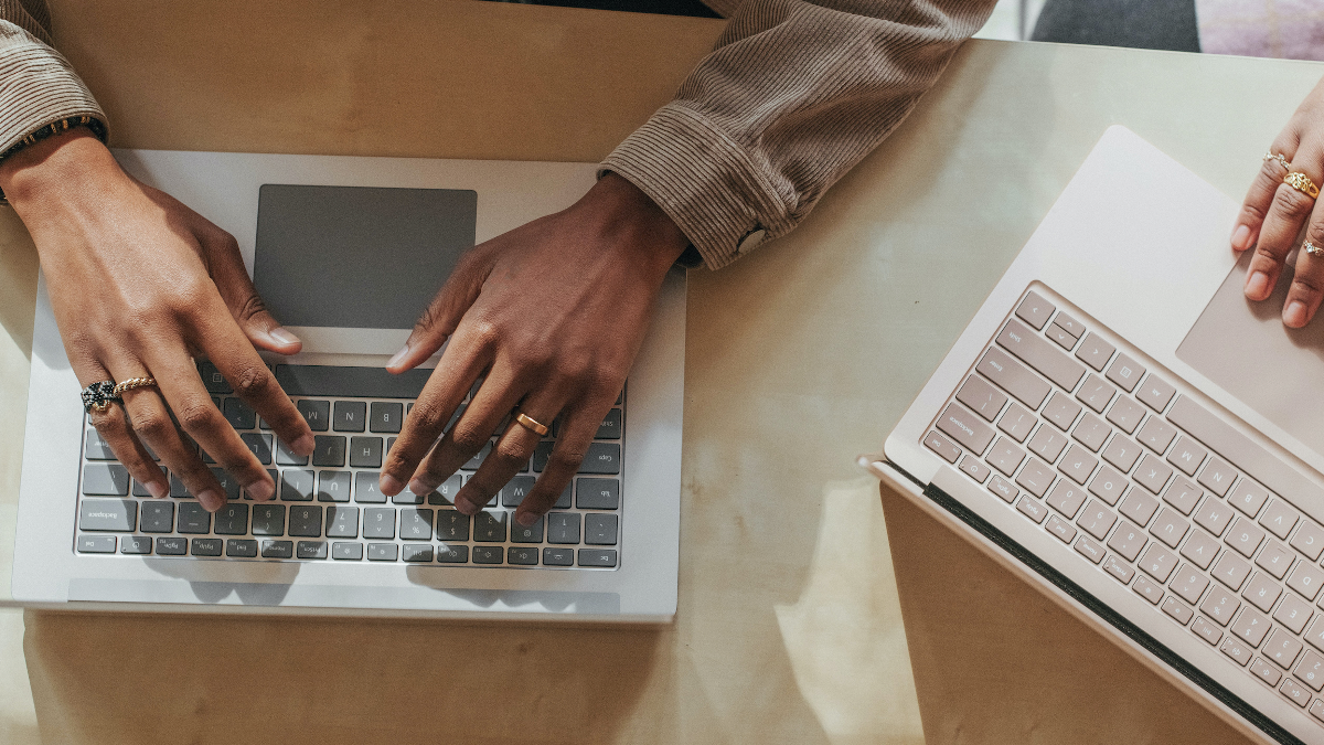 Two people seated at a table, intently typing on their laptops, illustrating a moment of productivity and teamwork.