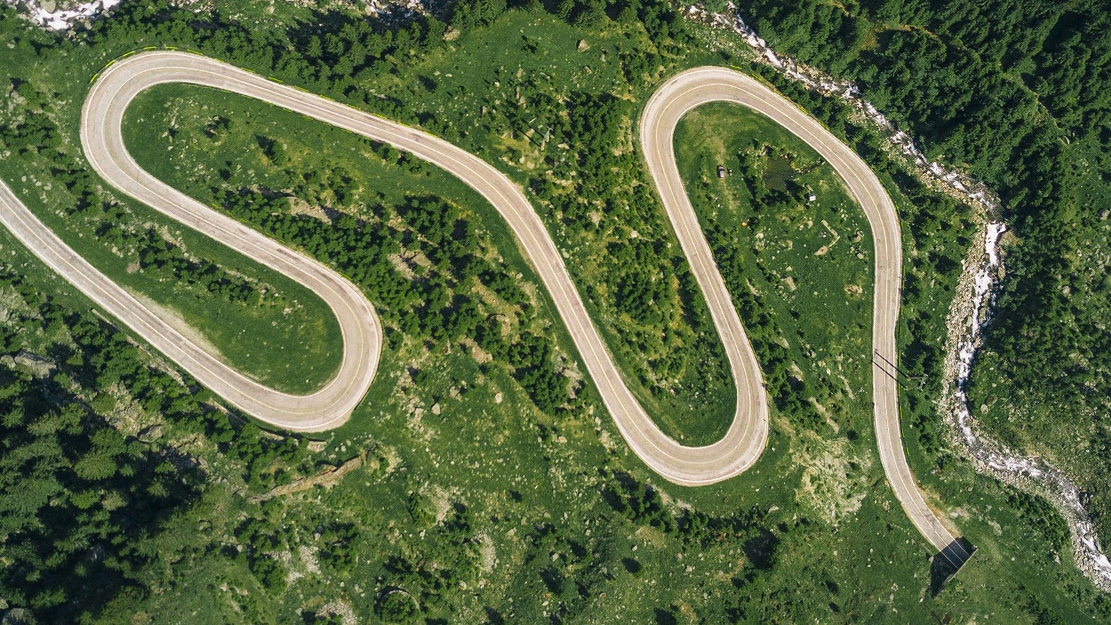 Aerial view of a winding road forming an ‘S’ shape through a green landscape.