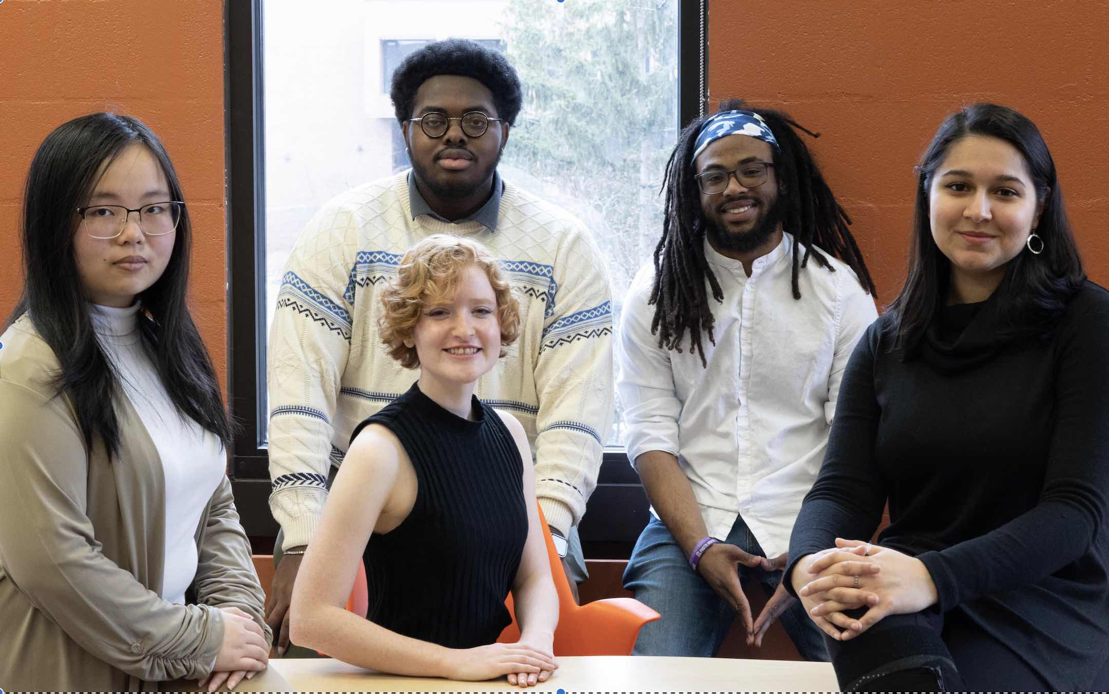 5 people posing for an image, behind an orange wall.