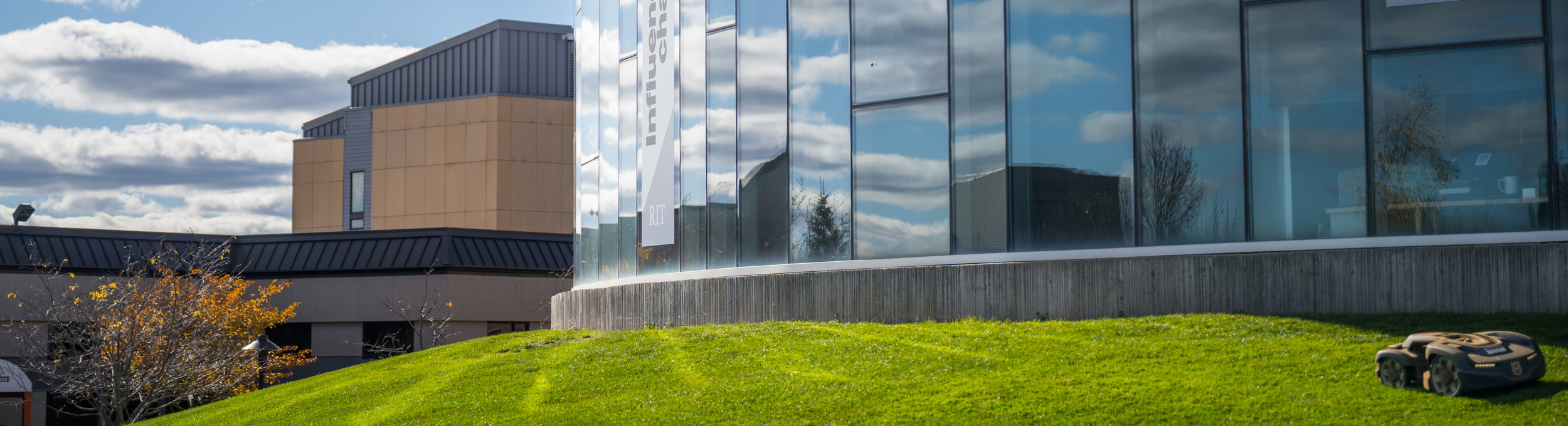 University Services Center building glass facade and lawn with lawnmower robot husqvarna sky clouds autumn global village