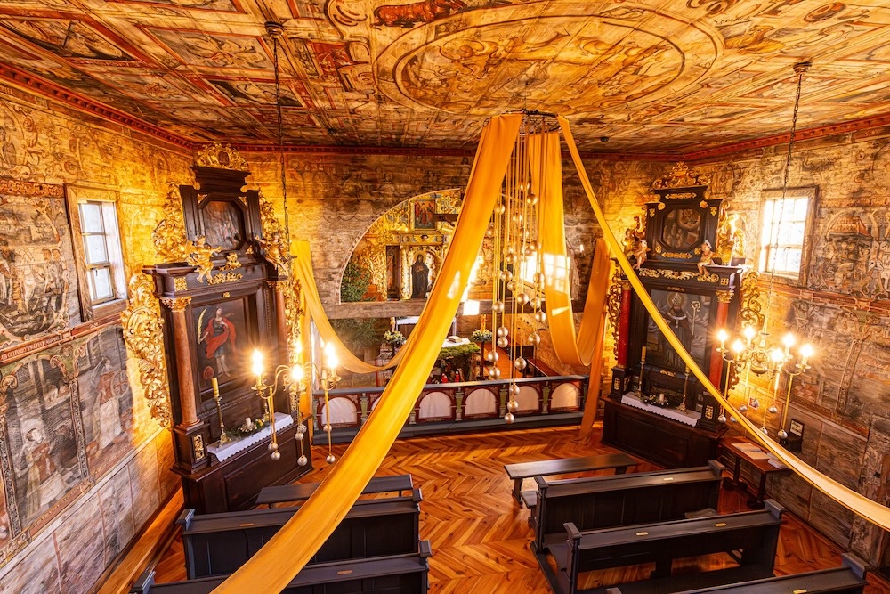 a color photograph of the interior of an ornate   handpainted walls with golden ribbons strung from the ceiling in a historic church chapel