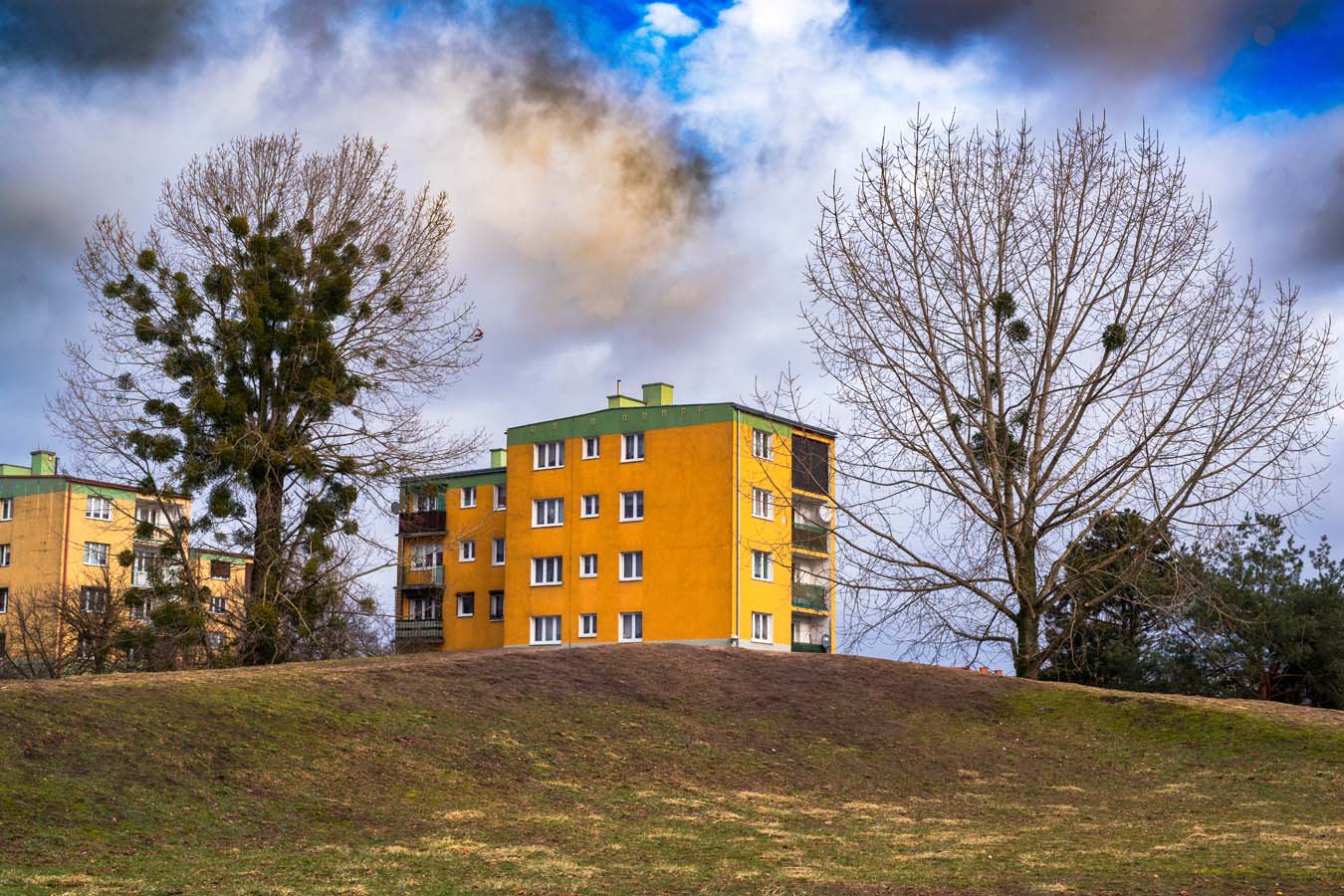 a color photograph of an austere four story block building painted bright orange with a green roof against a cloudy sky.