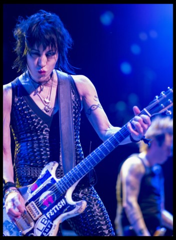 Color photograph of musician Joan Jett playing a guitar on stage.