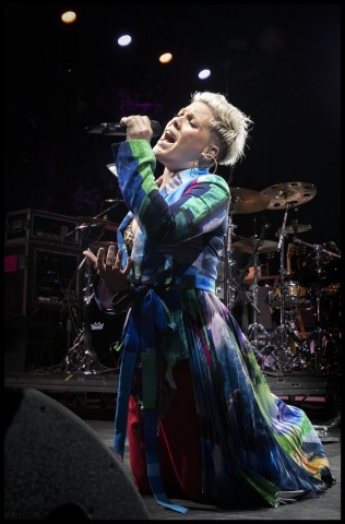 Color photograph of musician Pink singing into a handheld microphone on stage.