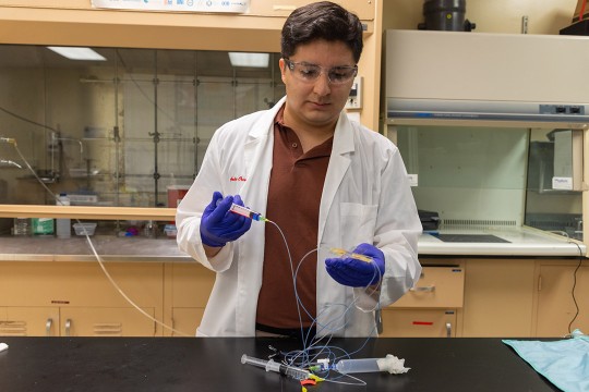 a student is standing at a lab table testing micron glass beads to improve visualization under fluorescent microscopes.