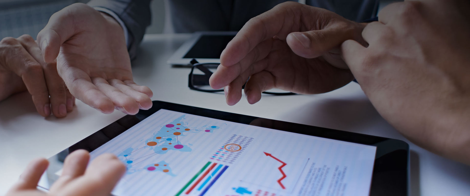 Two individuals analyzing data charts and graphs on a digital tablet, with a focus on hands and the tablet screen displaying colorful statistical information.